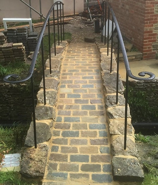 A cobbled path between stone walls with curled wrought iron handrails