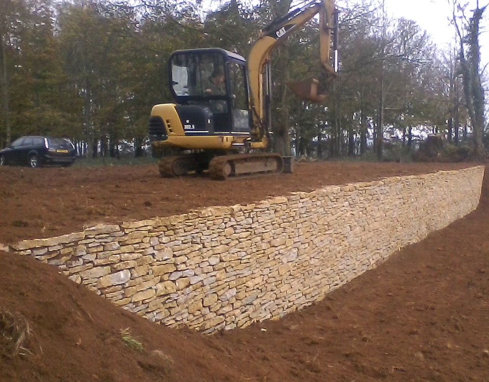 A mini excavator above a newly built dry stone retaining wall
