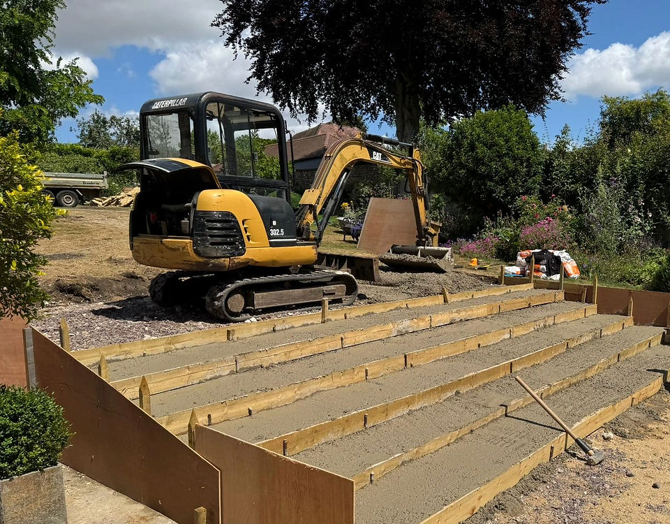 A mini excavator beside newly formed stone steps being shuttered and concreted in a garden