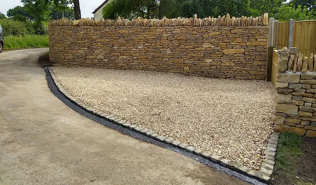 A gravel drive edged by a tall dry stone wall