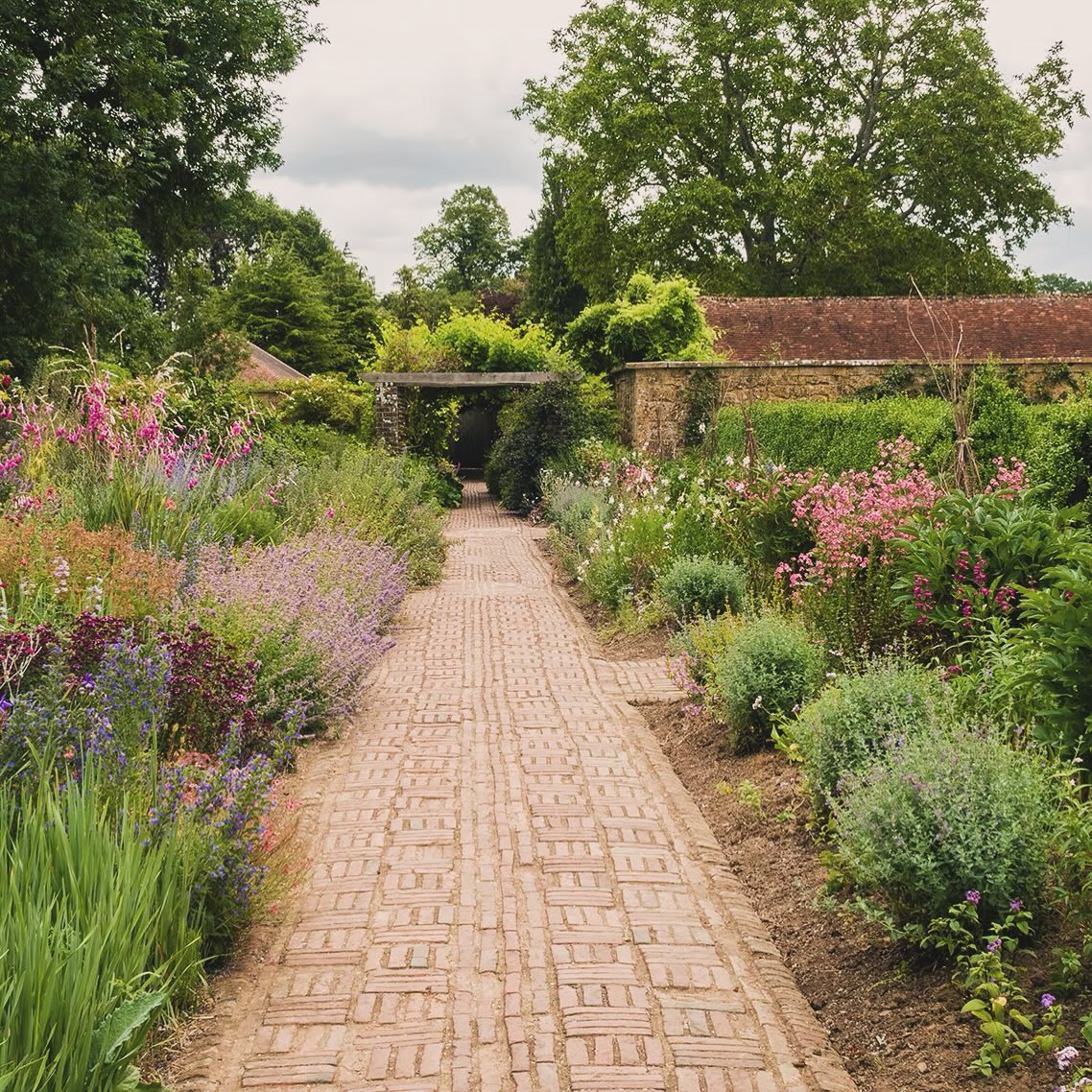 A brick path running between deep flower borders in a landscaped garden