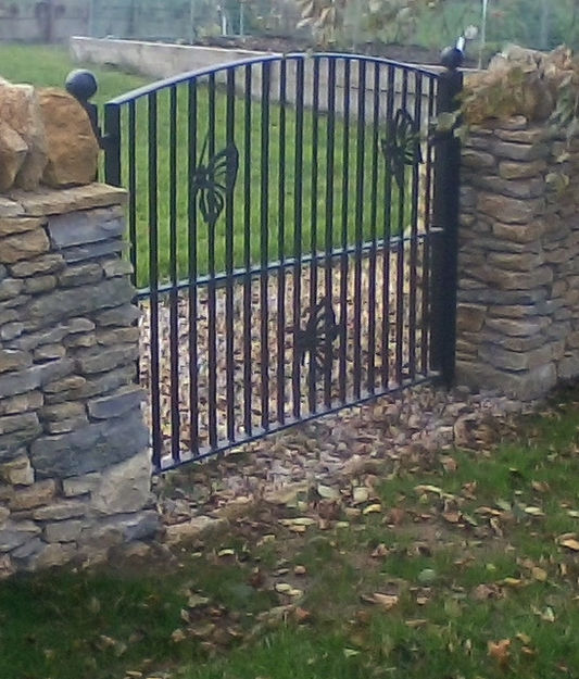 A wrought iron garden gate with leaf motifs between stone gate piers