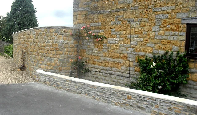 A stone retaining wall with a climbing rose beside a drive