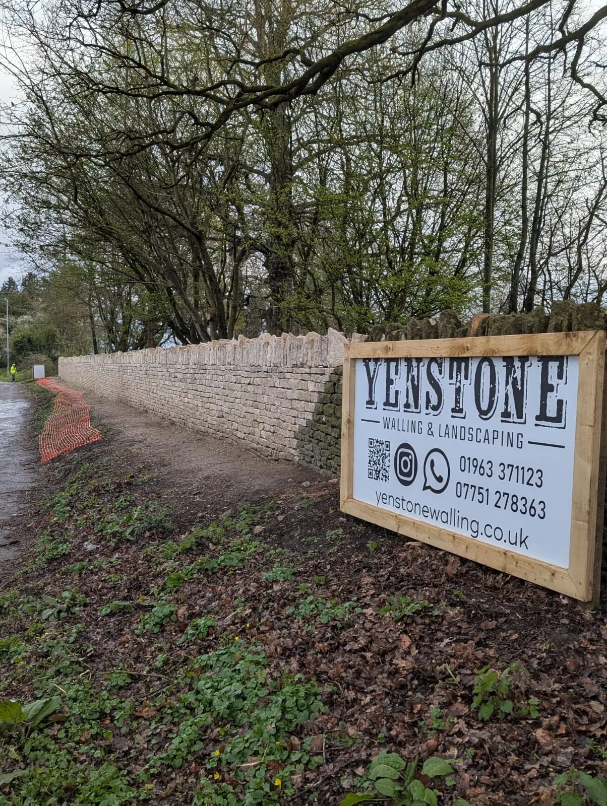 A long pale stone wall beside a country lane and a Yenstone sign