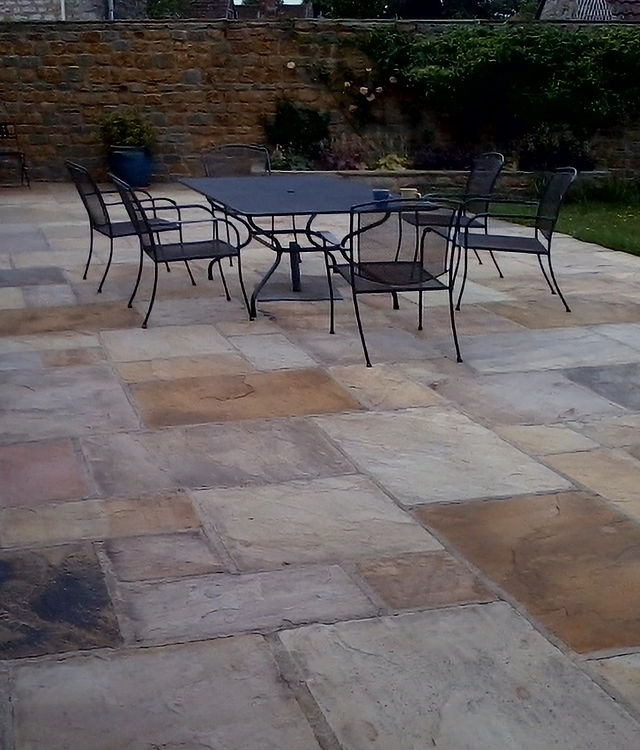 A sandstone patio with a metal table and chairs against a stone wall