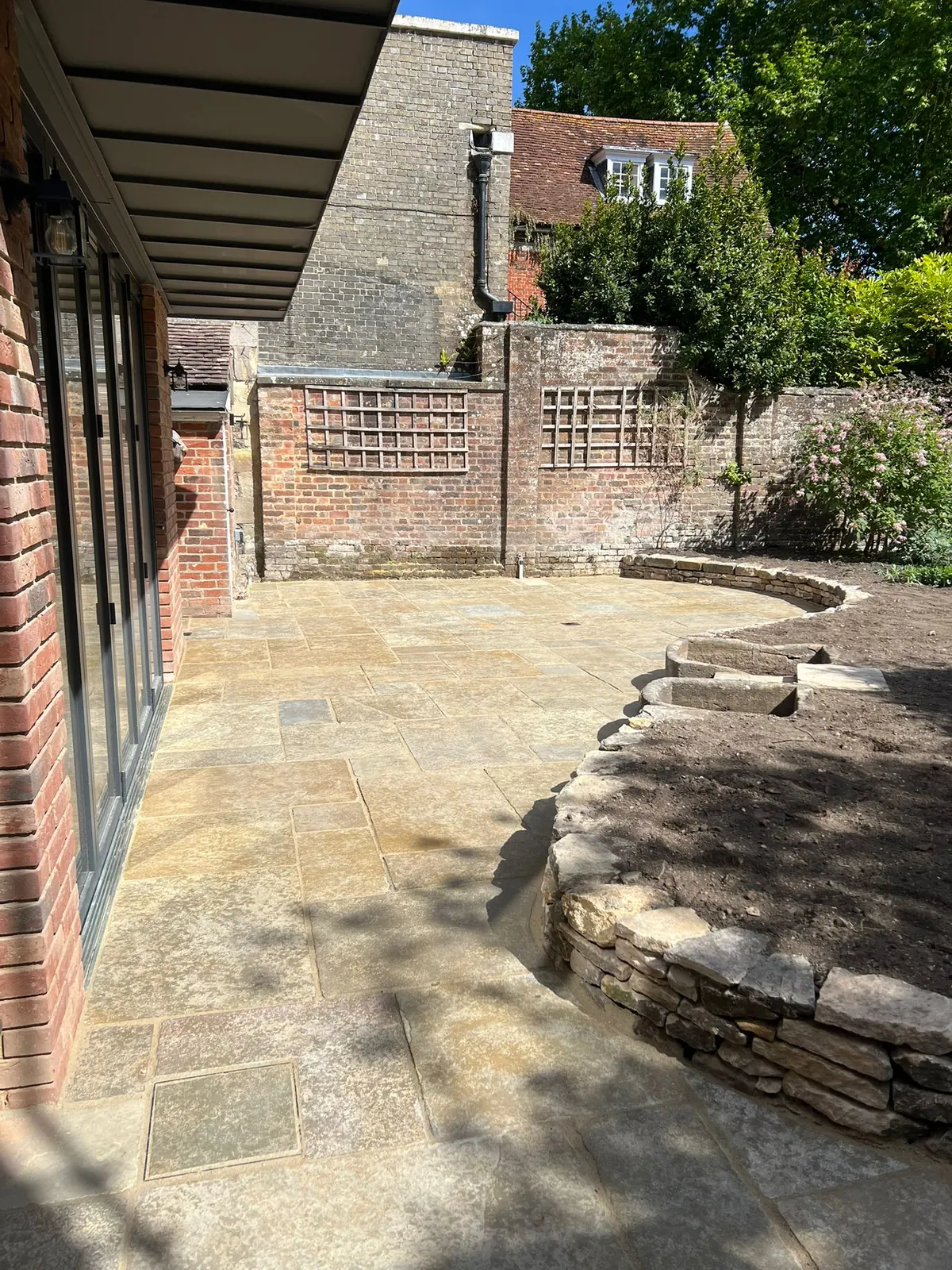 A sandstone patio beside a raised curved stone planting bed