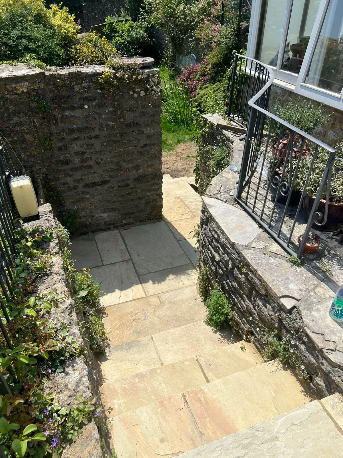 Sandstone steps with an iron handrail between stone garden walls