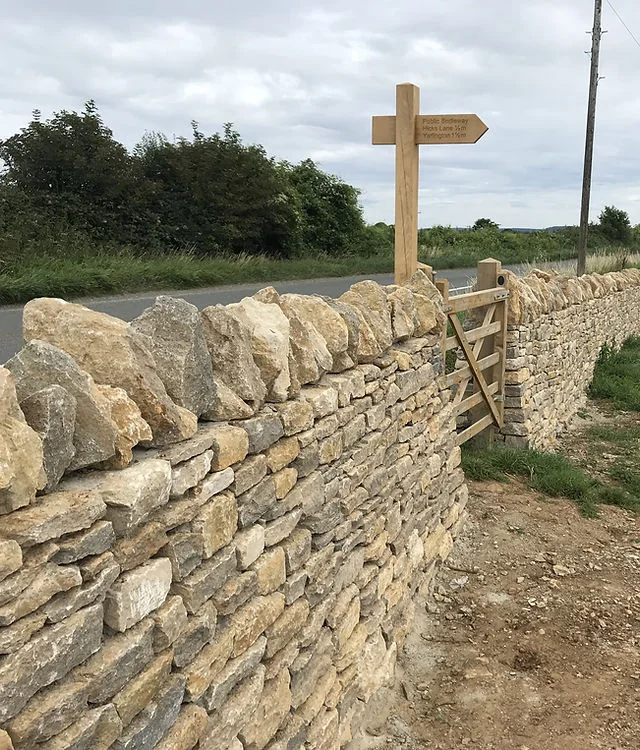 A newly built dry stone wall beside a lane with a wooden signpost