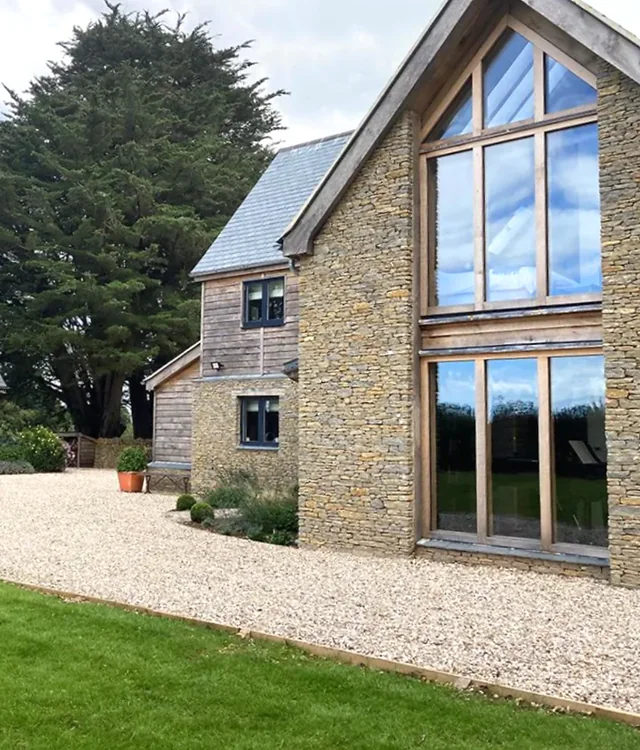A stone and oak house with a tall glazed gable and gravel drive