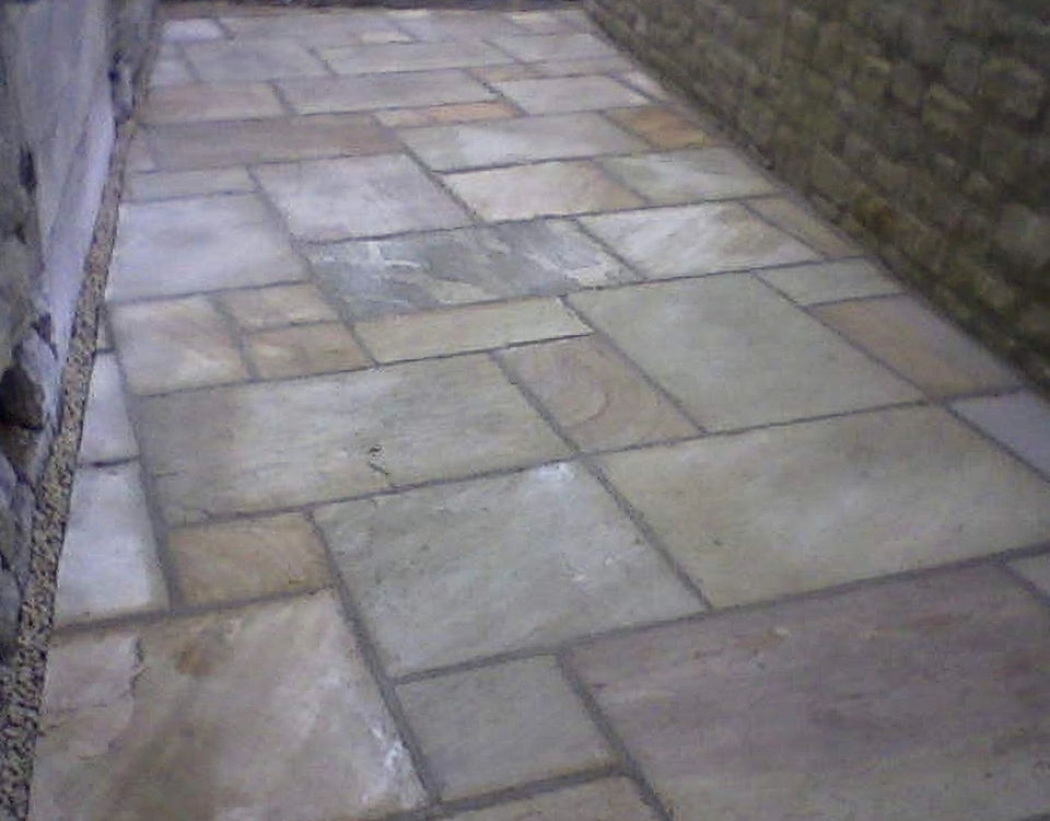 Irregular sandstone paving laid as a path beside a stone wall
