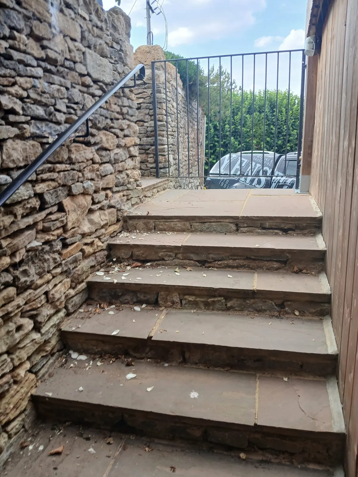 Stone steps with a black iron handrail between traditional stone walls