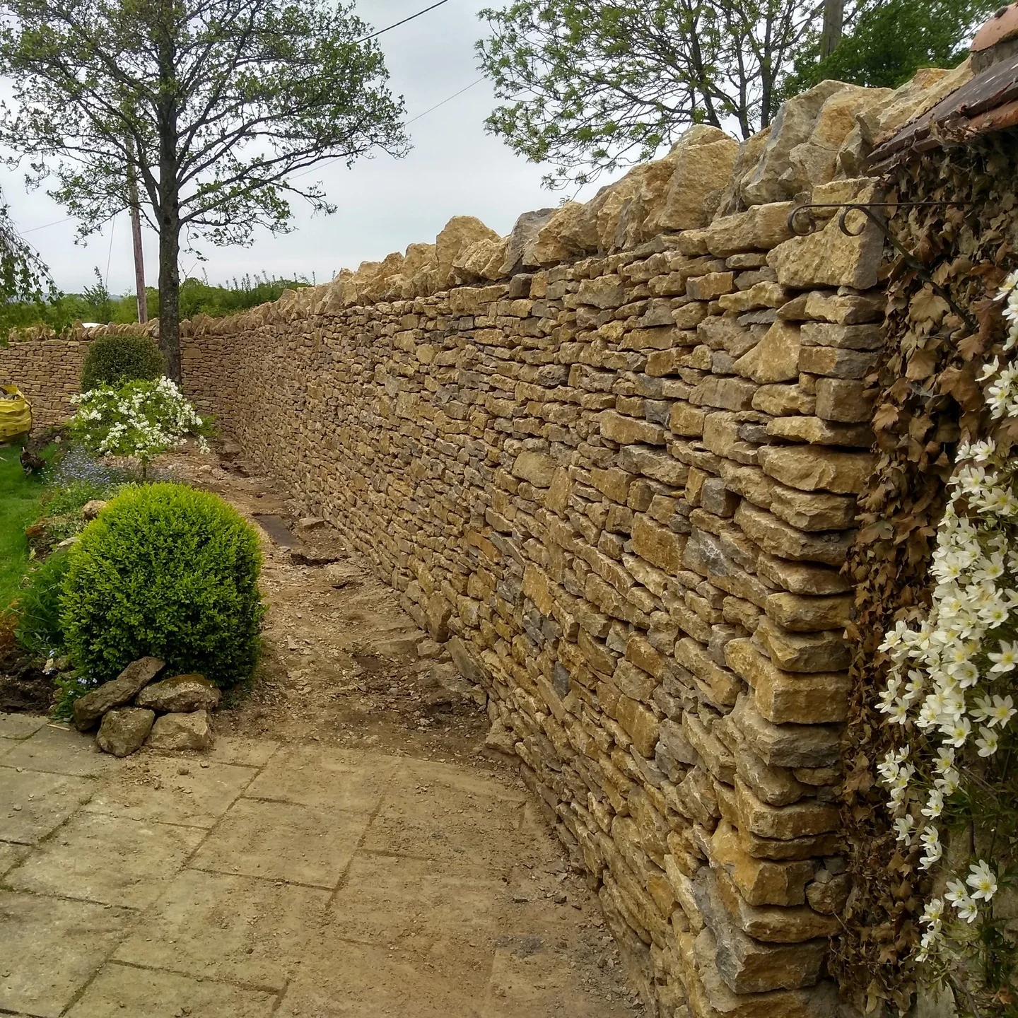 A dry stone wall running beside a planted border and a paved path