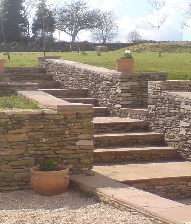 Stone steps and low retaining walls rising through a garden, with terracotta pots
