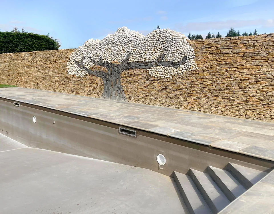 A dry stone wall with a tree carved in relief behind a swimming pool
