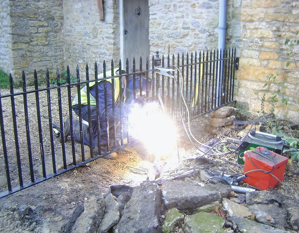 New wrought iron railings being welded on site beside a stone building